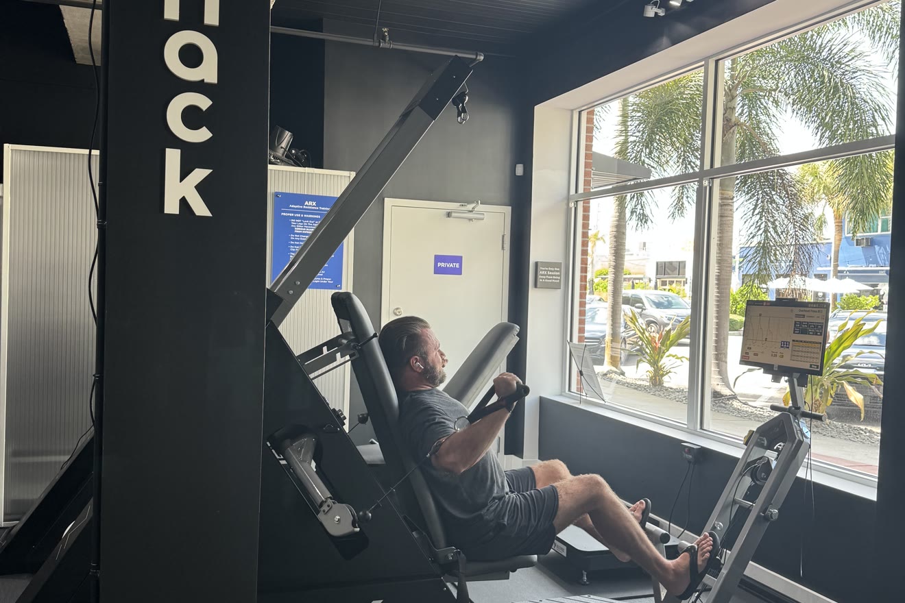 Member doing a leg press on the ARX machine beside BioHack Studios branding